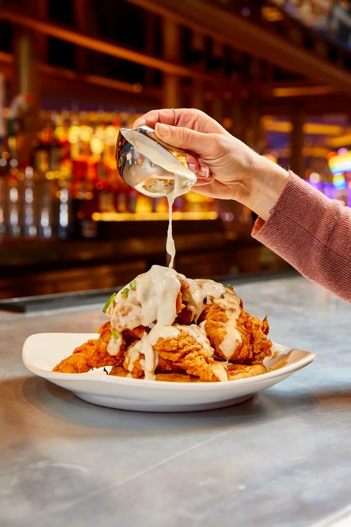 Golden fried chicken and waffles with creamy gravy being poured.