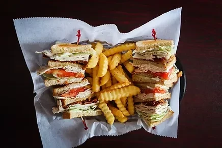 Two club sandwiches and crinkle fries in a parchment-lined basket.