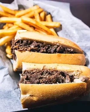 Close-up of a cheesesteak sandwich cut in half with french fries.