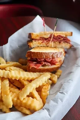 Close-up of a Reuben-style sandwich and crinkle-cut fries in a basket.