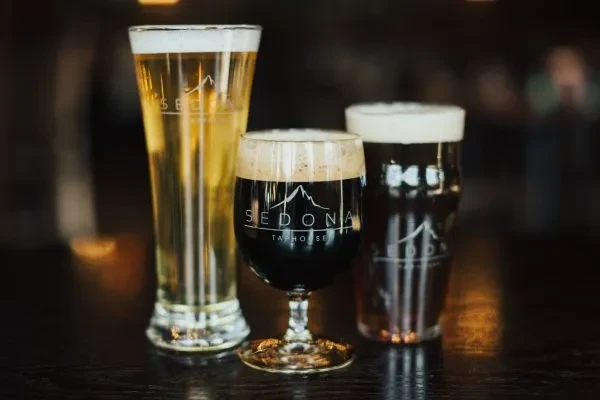 Three glasses: light pilsner, dark stout, amber ale, with Sedona logos.