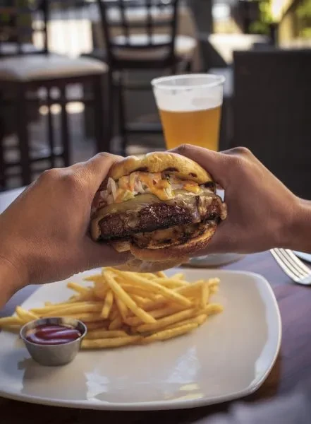 Gourmet burger held by hands, with fries and beverage in restaurant.