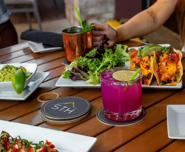 Colorful drinks, tacos, and guacamole on a restaurant patio table.