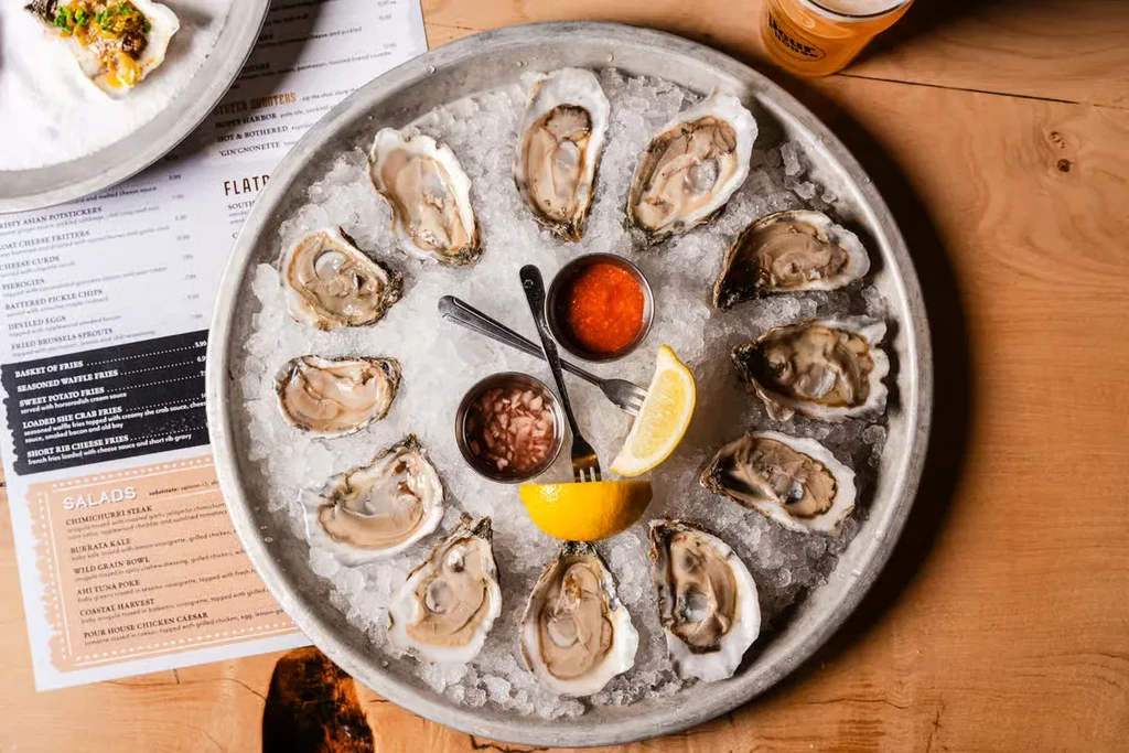 Platter of shucked oysters on ice with dipping sauces and lemon.