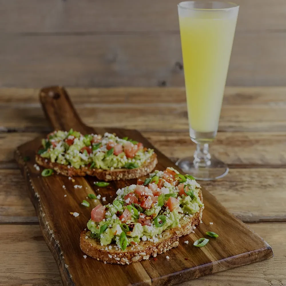 Avocado toast, tomatoes, cheese, green onions, and a yellow beverage.
