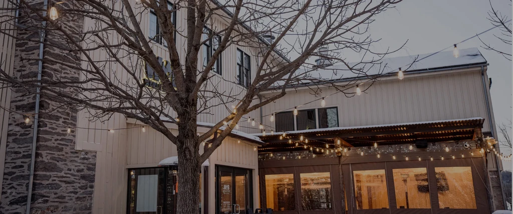 Snowy restaurant exterior with stone facade, white siding, and illuminated string lights.
