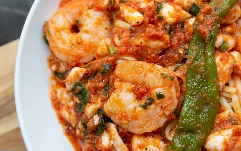 Close-up of shrimp pasta in tomato sauce with herbs and chili.