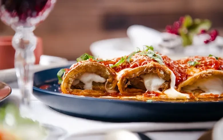 Three cheese-filled eggplant/zucchini rolls with tomato sauce, grated cheese, herbs.
