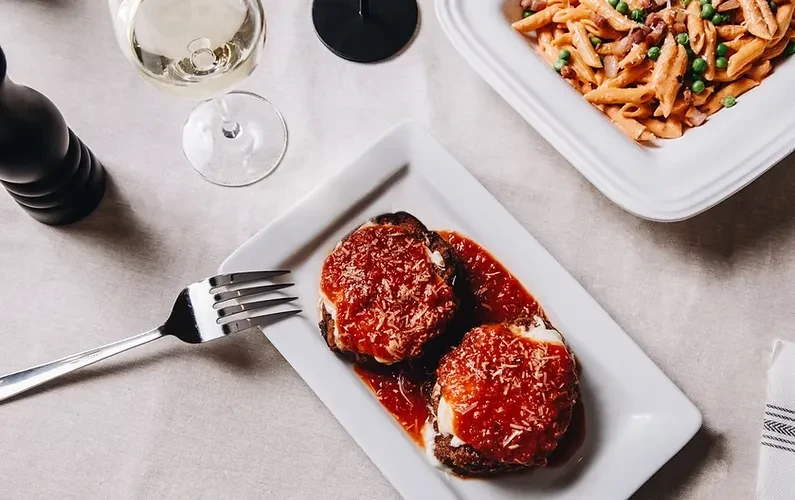 Dining table overhead: meat dish, red sauce, pasta, and wine.
