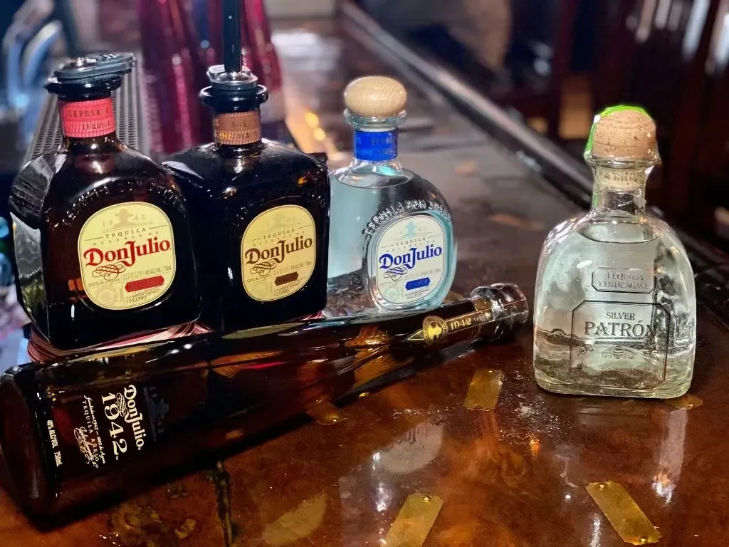 Five Don Julio and Patrón tequila bottles on a wooden bar.