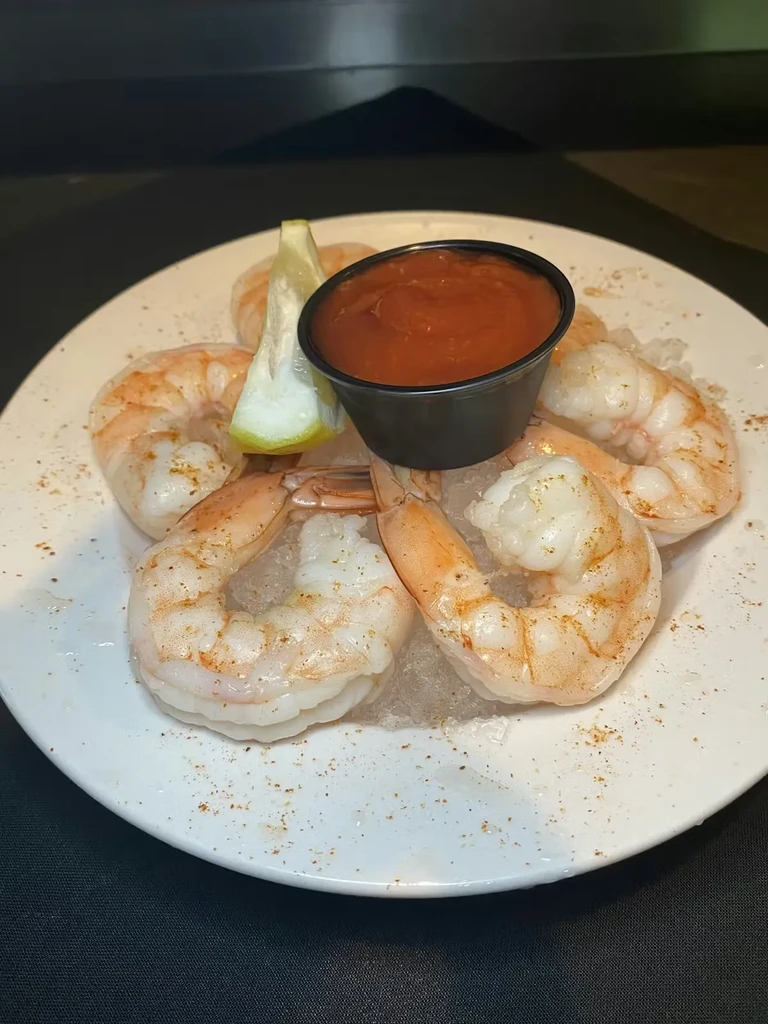 White plate with shrimp cocktail, ice, sauce, lemon, and seasoning.