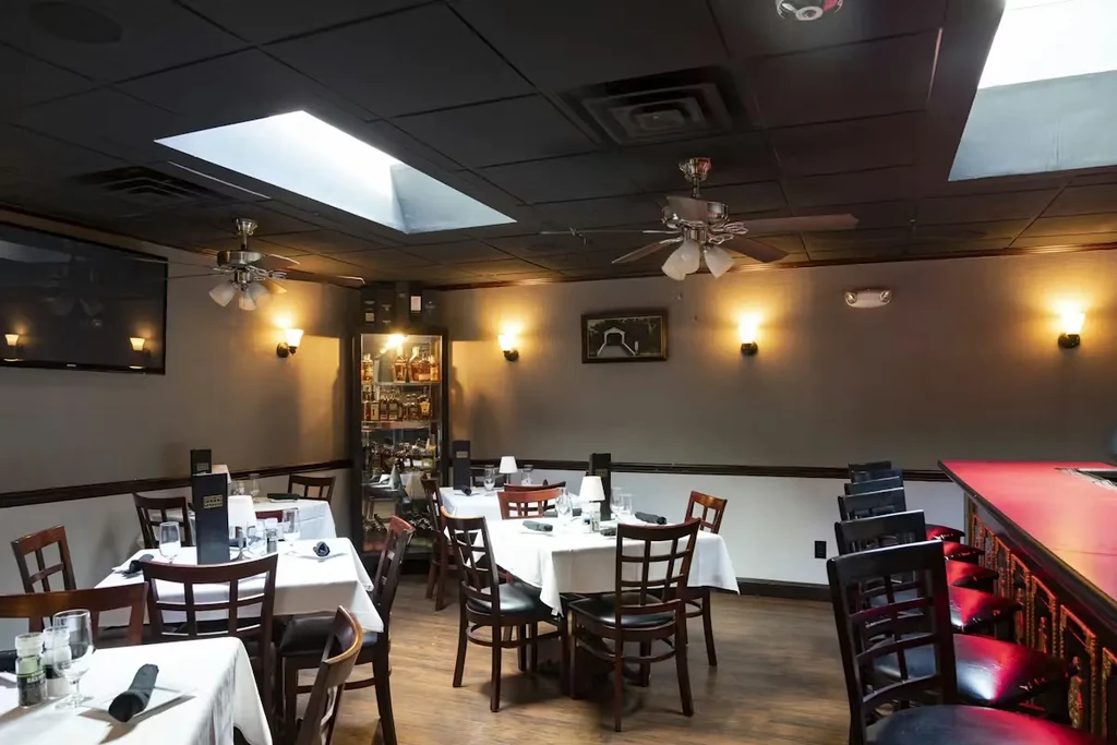 Empty restaurant interior with set tables, a bar, skylights, and warm lights.