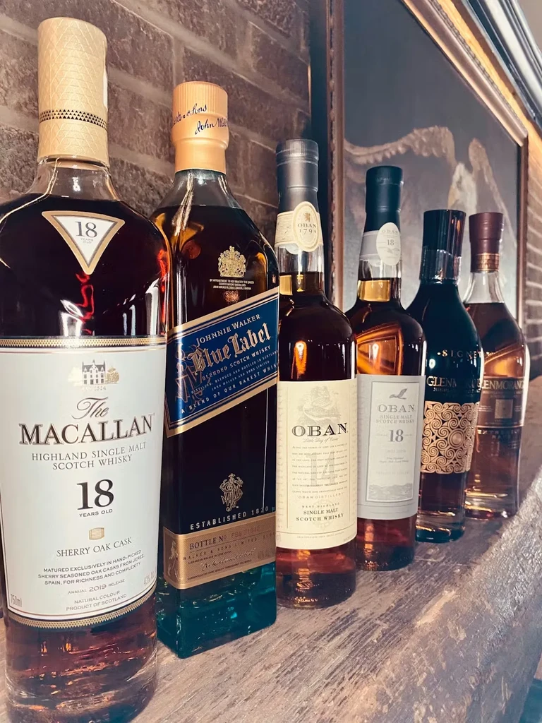 Six high-end whiskey bottles, Macallan and Johnnie Walker, on a rustic bar.