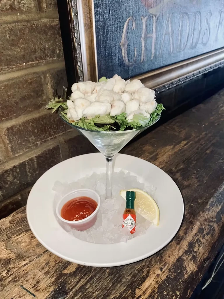Seafood cocktail in martini glass, lettuce, crushed ice, sauce, lemon.