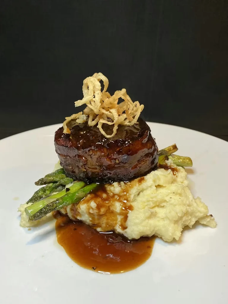 Plated beef, mashed potatoes, asparagus, fried onions, and dark sauce.