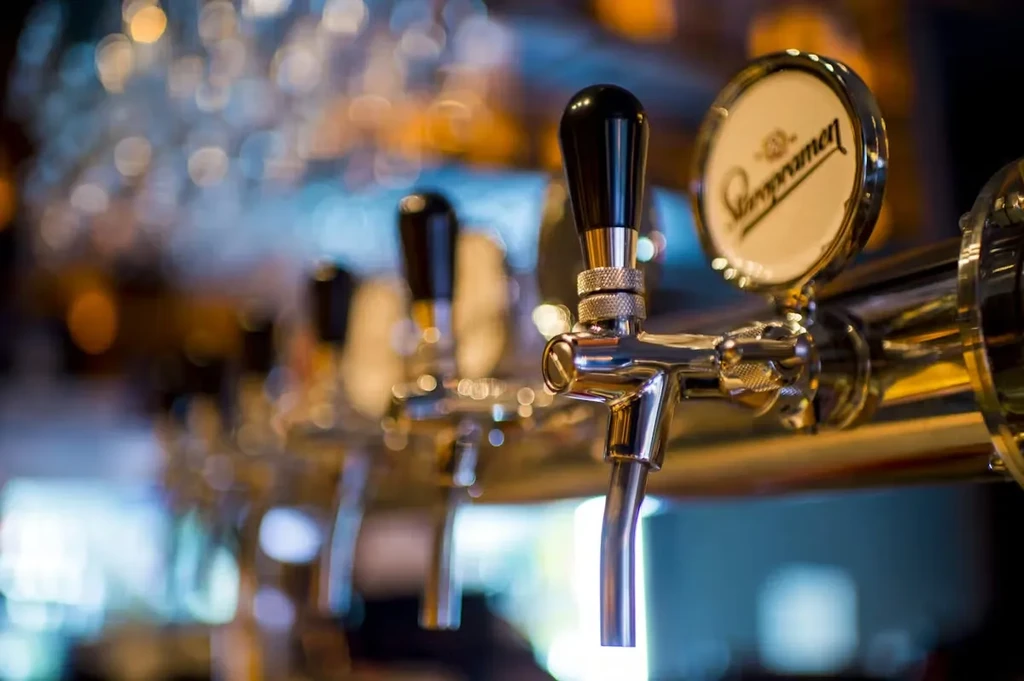 A clear Staropramen beer tap with other taps and bokeh lights.