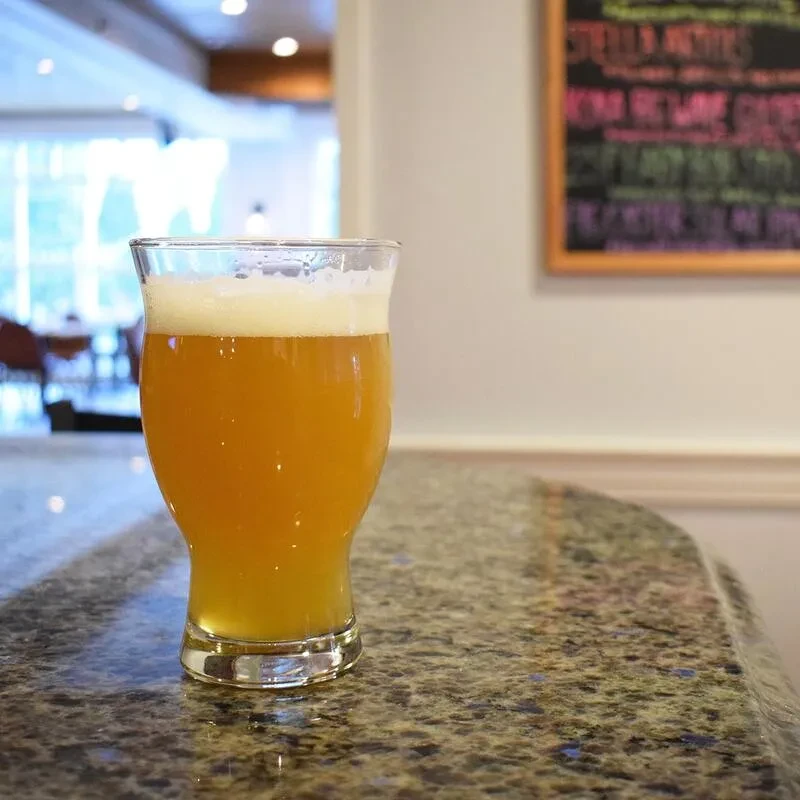 Frothy glass of amber beer on a granite counter near a chalkboard.