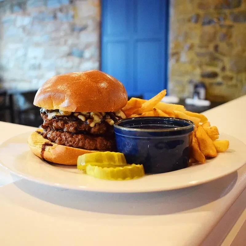 Double-patty burger, fries, pickles, sauce, against a rustic blue door background.