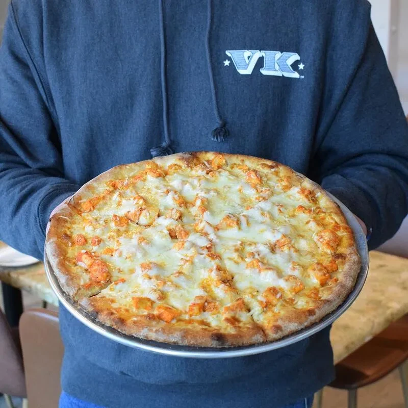 Person holding a large pizza with melted cheese and spicy chicken.