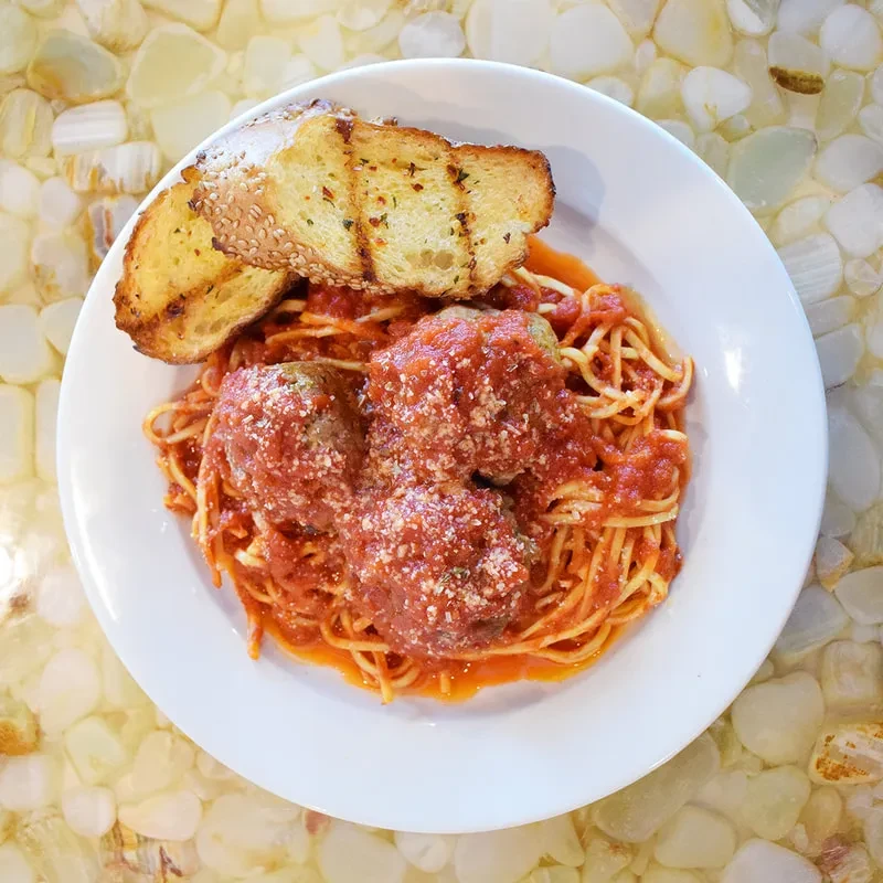 A plate of spaghetti and meatballs with cheese and garlic bread.