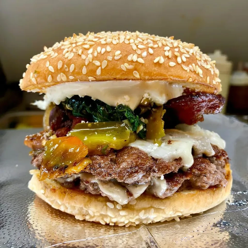 Close-up of a gourmet burger with melted cheese, bacon, and vegetables.