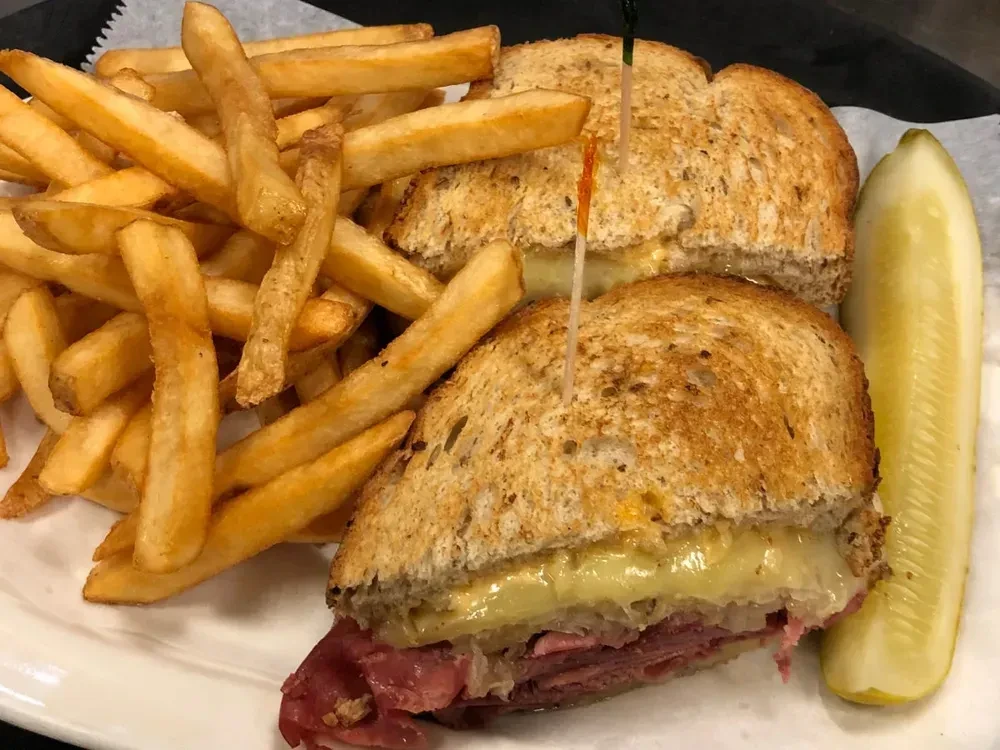 Reuben sandwich, golden fries, and a dill pickle on a plate.