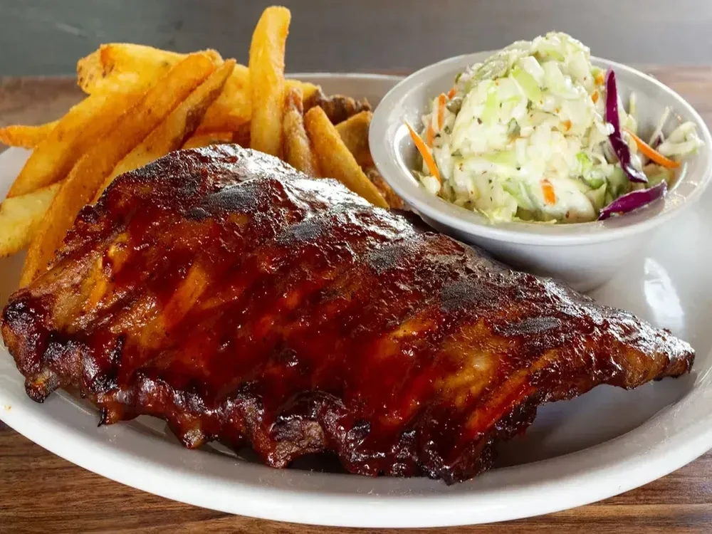 Close-up of BBQ ribs, steak fries, and coleslaw on a white plate.