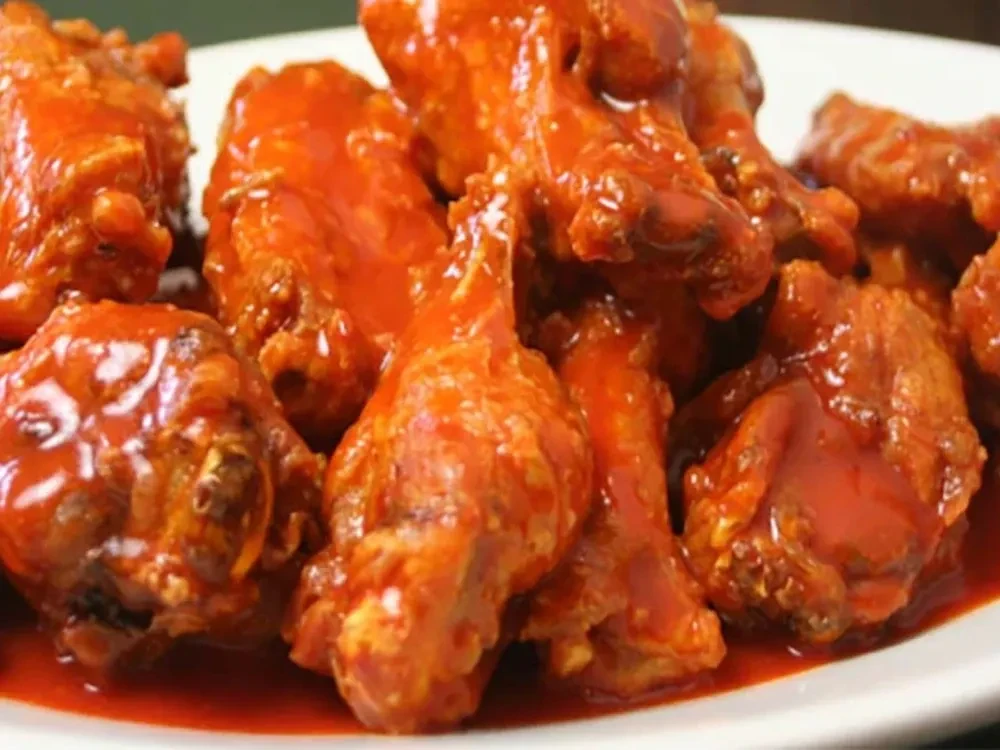 Serving of hot buffalo wings coated in orange sauce on white plate.