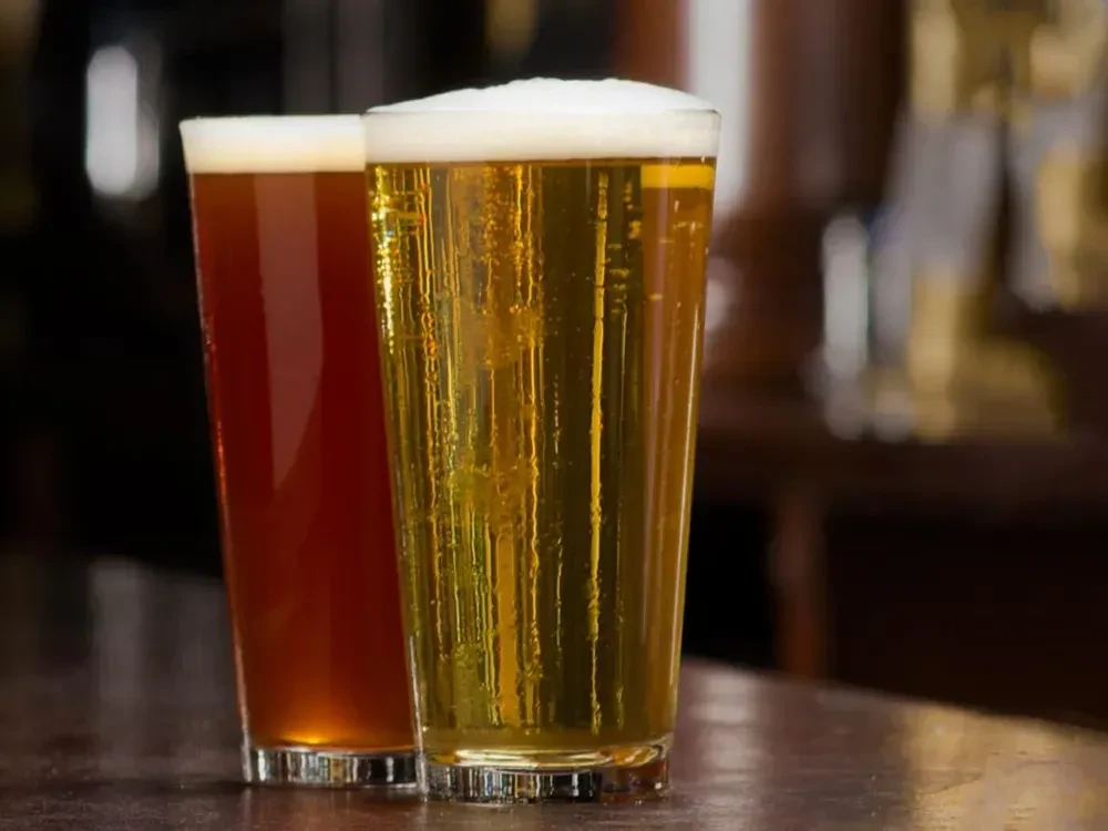 Two pints of amber and golden beer on a dark wooden bar.