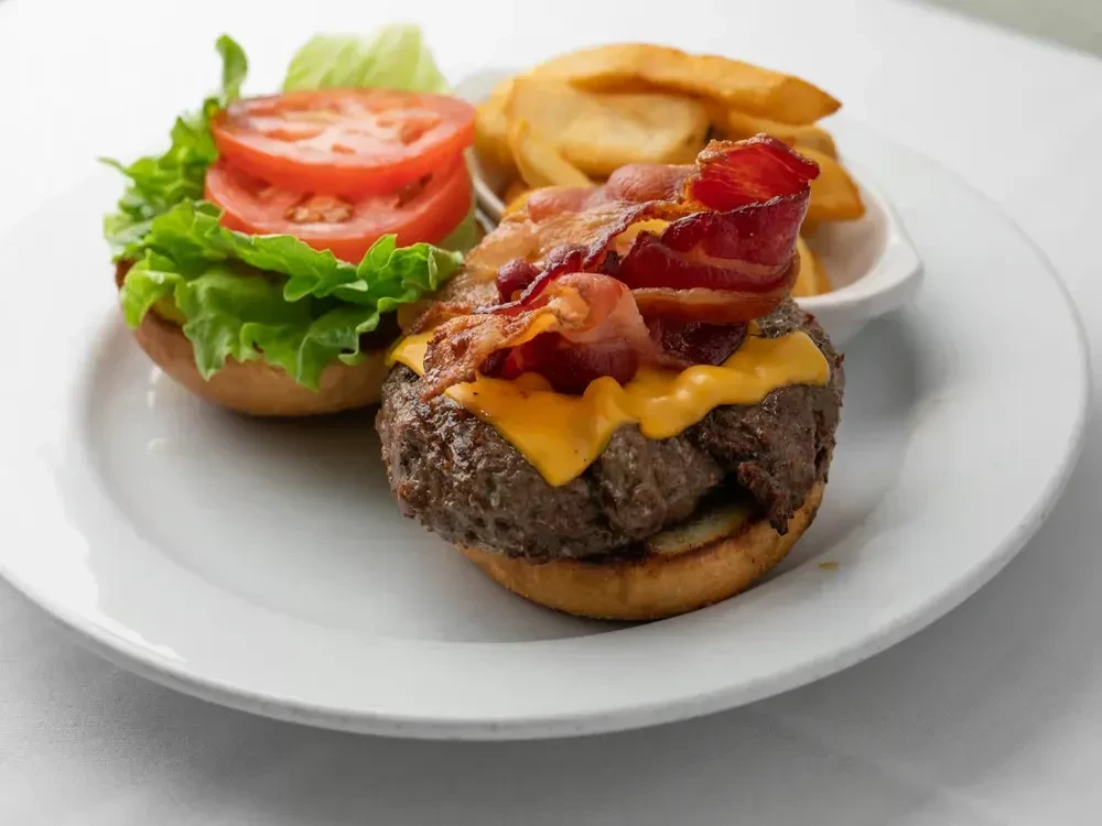 Open-faced bacon cheeseburger with melted cheese, lettuce, tomato, and fries.