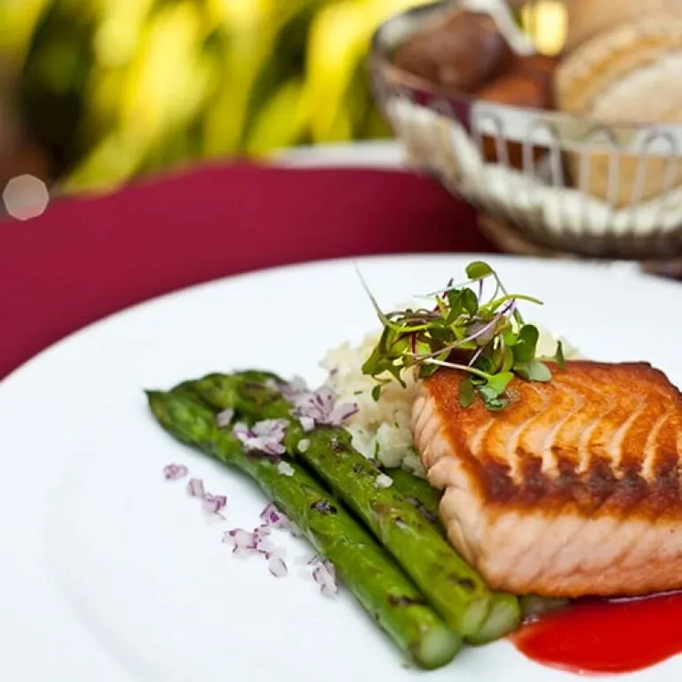 Seared salmon, asparagus, rice, and red sauce on a white plate.