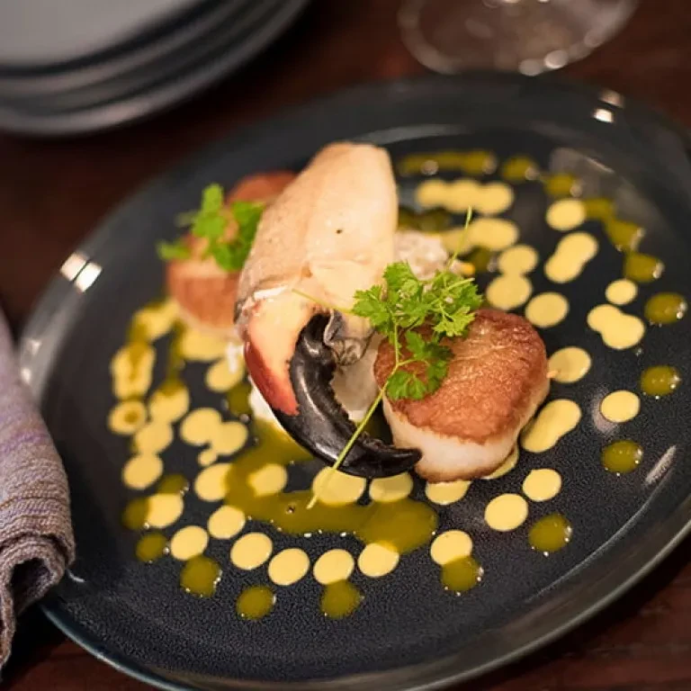Cooked crab claw and seared scallops with sauces, garnished on dark plate.