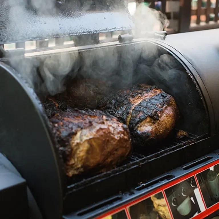 Two dark, charred roasts smoking in an industrial smoker.