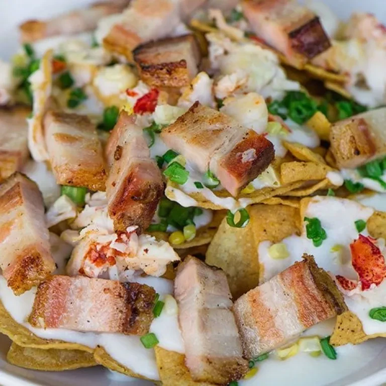 Crispy nachos topped with pork belly, creamy sauce, corn, and red pieces.