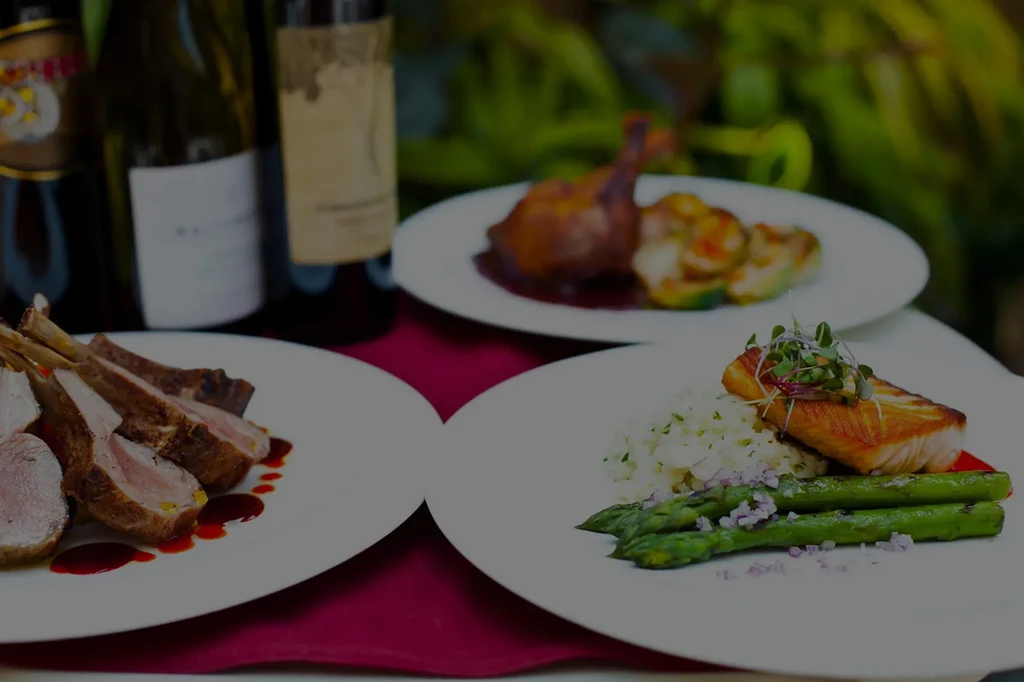 Plates of rack of lamb, salmon, duck, and wine bottles.