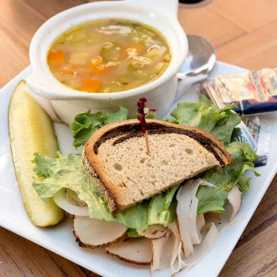 Noodle soup, deli meat sandwich, and dill pickle on a plate.