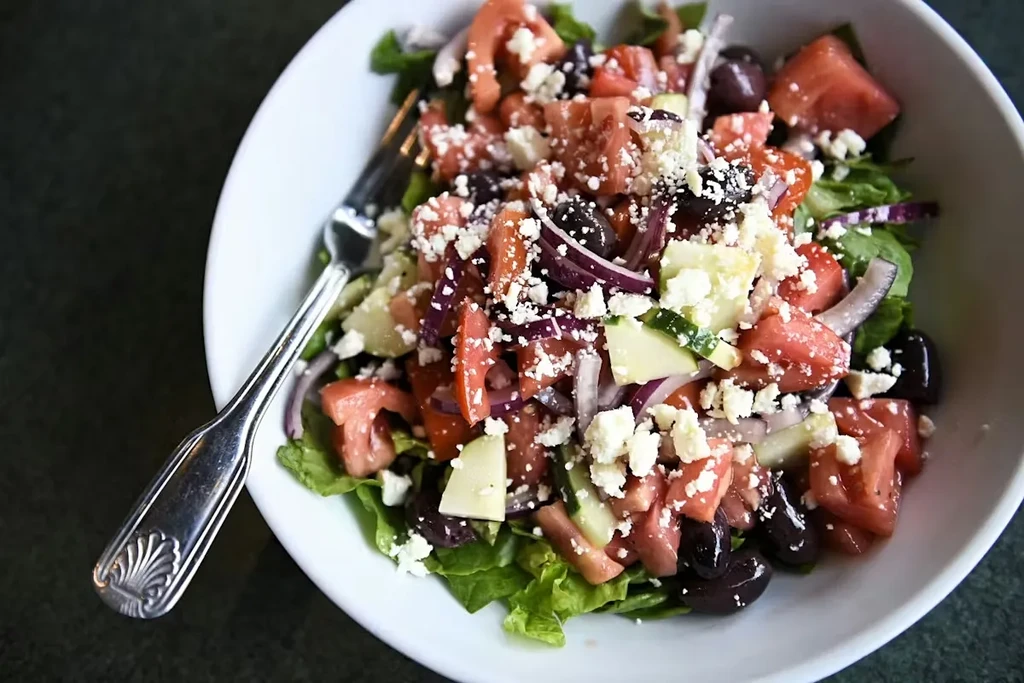 Close-up of a Greek salad with feta, olives, tomatoes, and a fork.