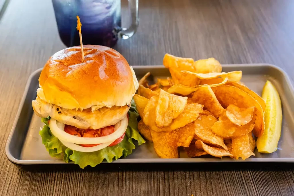 Burger, crispy chips, and pickle spear served on a dark tray.