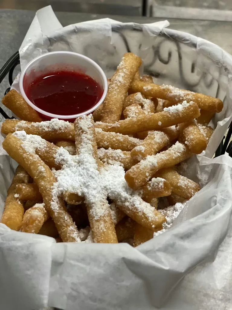 Black basket of powdered sugar churros and a red fruit sauce.