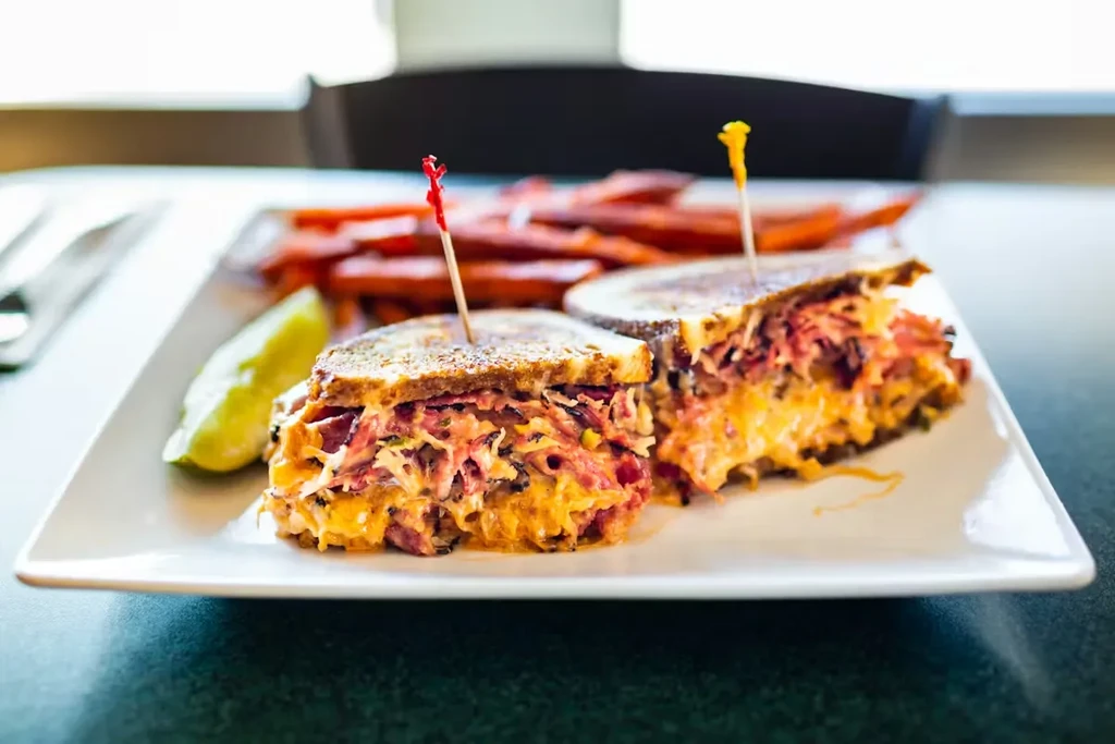 Hearty Reuben sandwich, cut in half, with a pickle and fries.