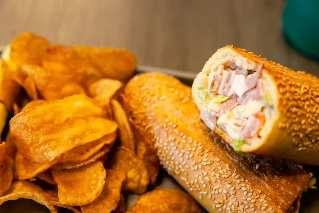 Golden-brown potato chips and two sesame ham and lettuce subs.