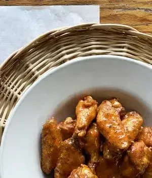 White bowl brimming with glossy orange-brown chicken wings.