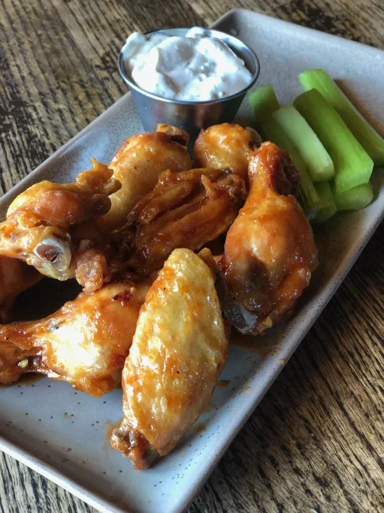 Plate of glazed chicken wings, white dipping sauce, and celery.
