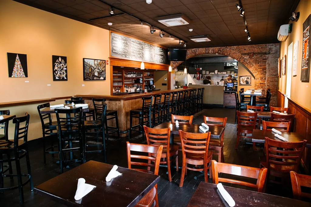 Well-lit restaurant interior with dining area, wooden bar, and chalkboard menu.