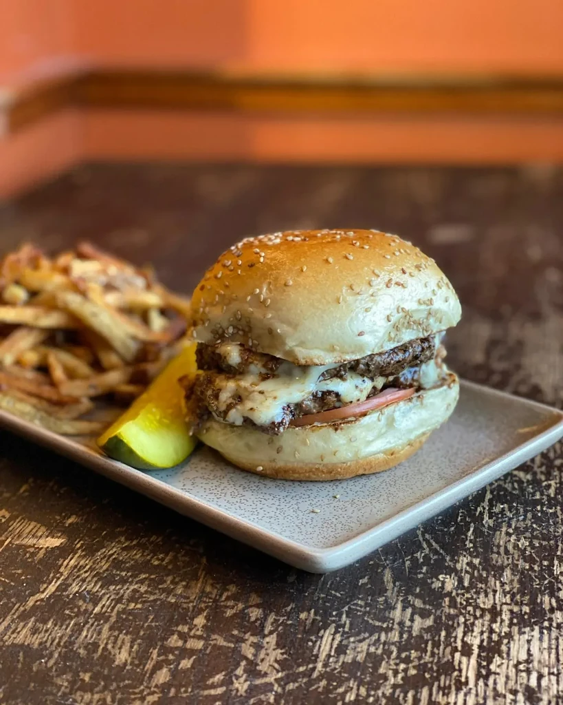 Double cheeseburger, fries, and pickle spear on a rustic wooden table.