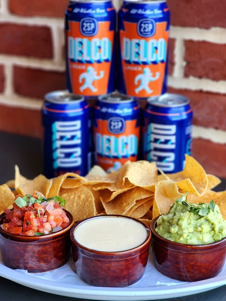 Tortilla chips with salsa, creamy dip, guacamole, and DELCO beer.