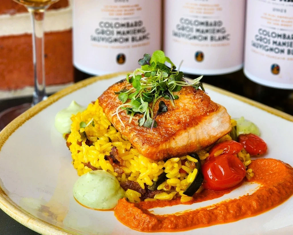 Elegant plate: seared fish, microgreens, yellow rice, tomatoes, two sauces.