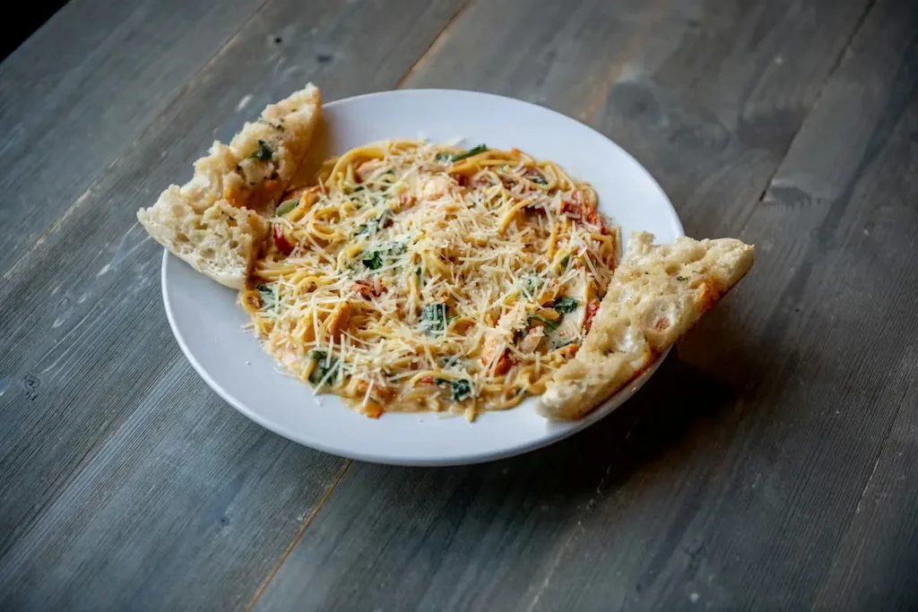 Plate of creamy pasta with vegetables, cheese, and garlic bread.