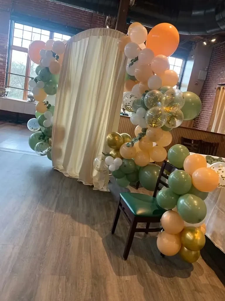 A colorful balloon arch frames an arched entryway in an empty venue.