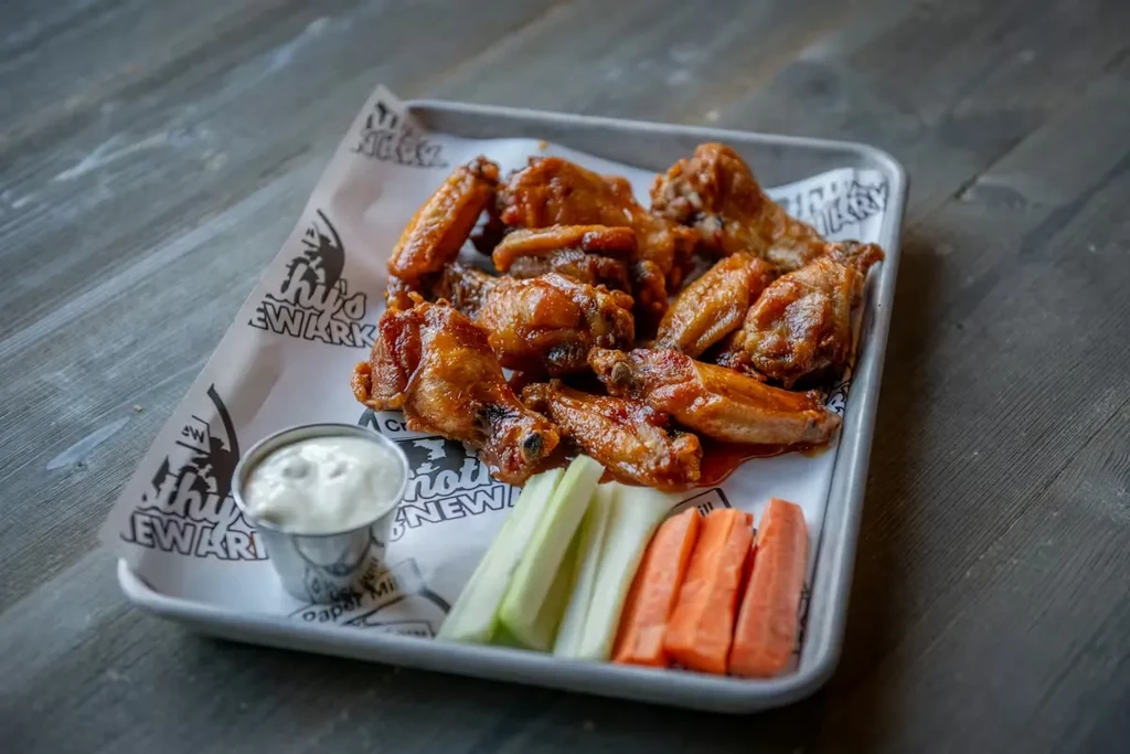 Golden-brown chicken wings with dipping sauce, celery, and carrots on a tray.